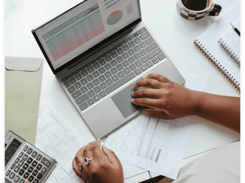 Foto de um investidor trabalhando em sua mesa, com ferramentas financeiras como uma xícara, notebook, calculadora e notas fiscais, ajustando dados financeiros e tomadando decisões estratégicas. Finanças e tomada de decisão.